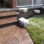 Stamped coloured concrete sidewalk with a new lawn and Armour Stone in the garden.
