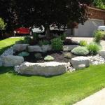 Armour Stone garden with river rock, mulch and shrubs in front yard.