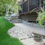 Finished Armour Stone retaining wall, sidewalk, and river rock landscaping.