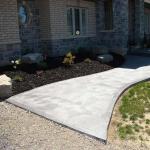 New Armour stone garden with black mulch next to a decorative concrete sidewalk.