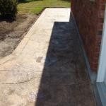 Coloured patterned concrete sidewalk along the side of a house.