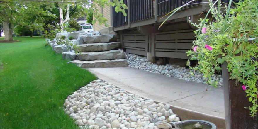 Armour stone retaining wall with stone steps and new concrete sidewalk with river rock.